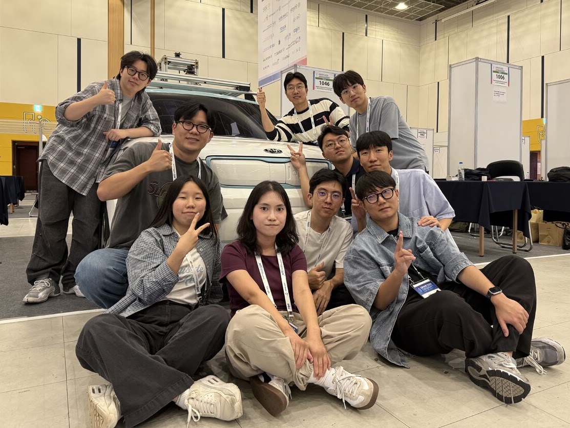 Group photo beside a vehicle demonstration at ISMAR 2025.